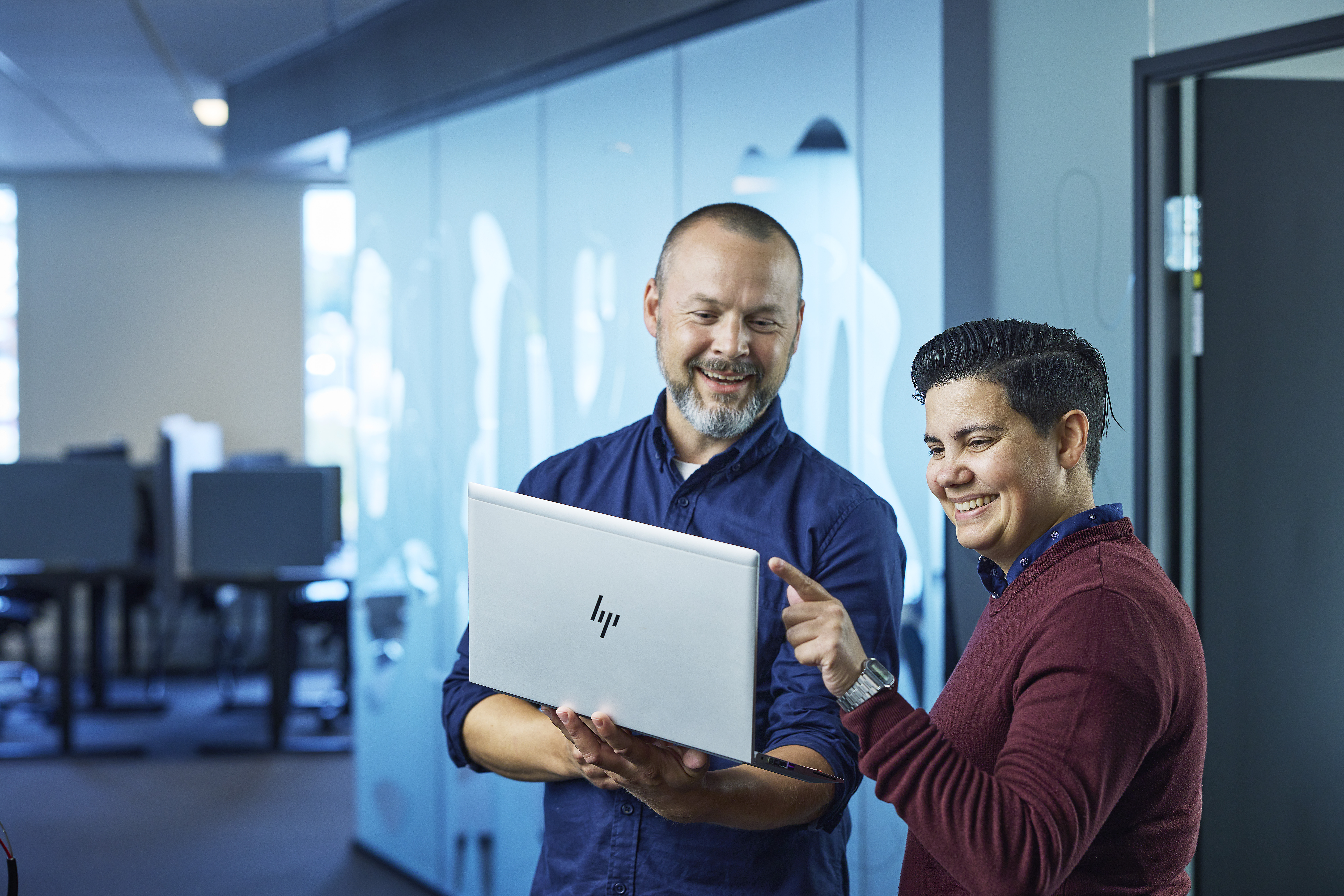 Kvinne og mann står i kontorlokale og ser på innholdet på en laptopskjerm.