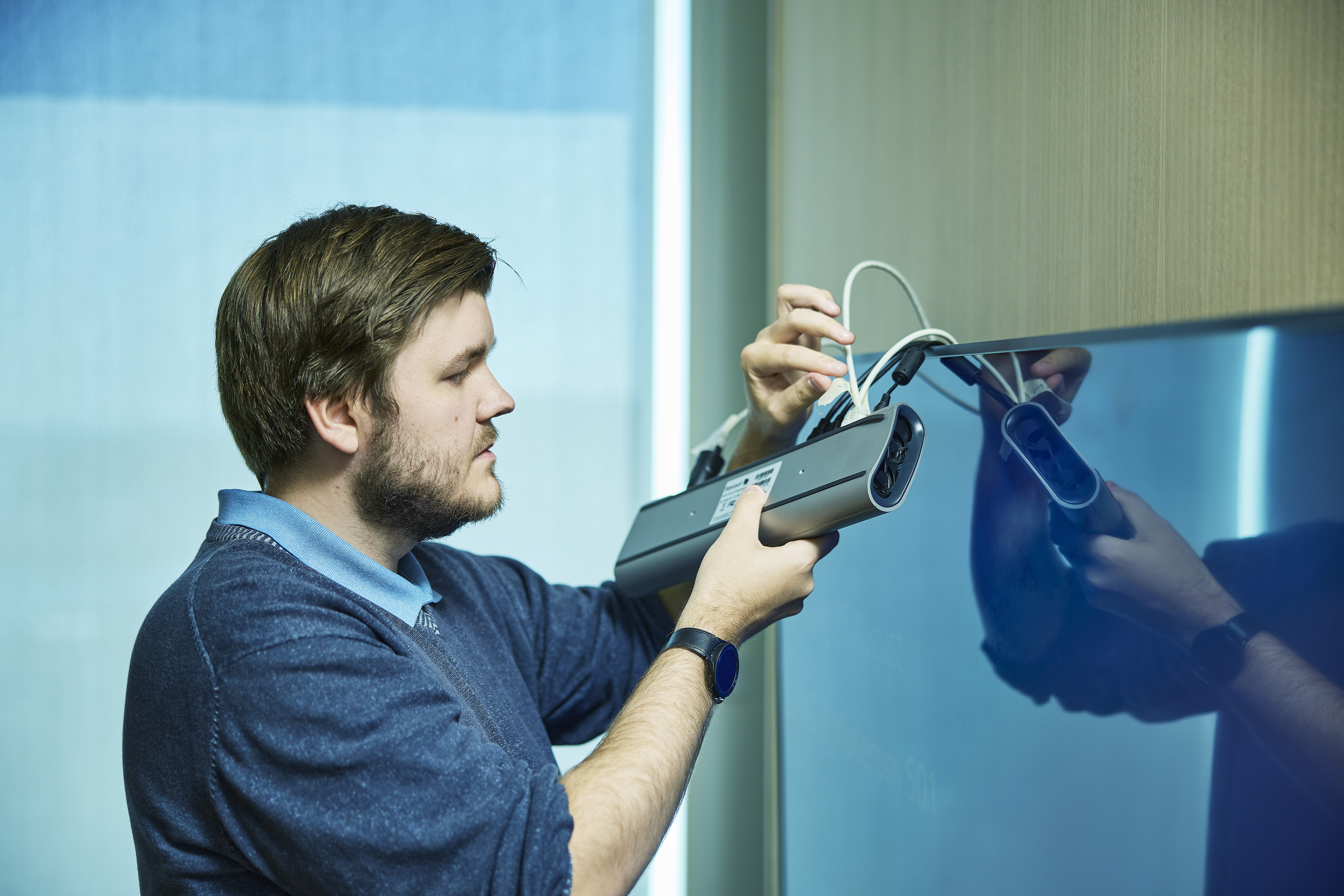 Mann kobler opp møteromutstyr foran en stor tv-skjerm. 